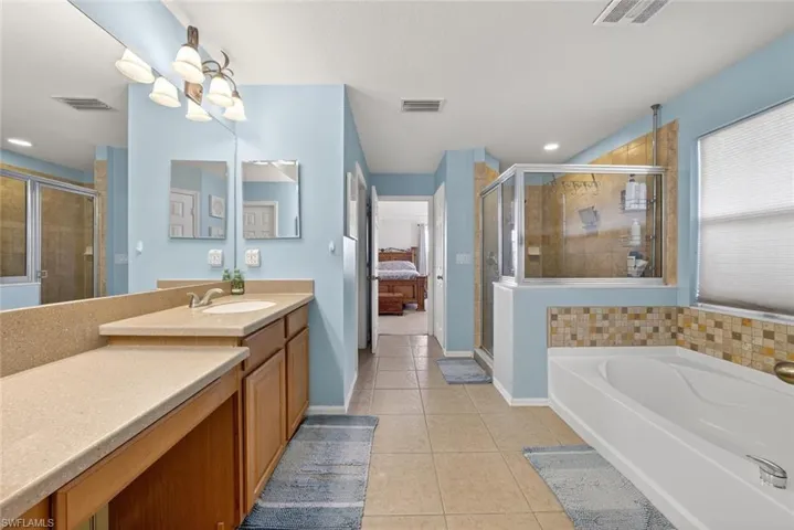 Ensuite bathroom featuring tile patterned flooring, dual vanity, a stall shower, a bath, and recessed lighting