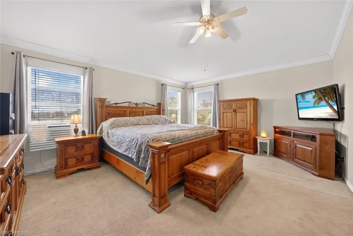 Primary bedroom featuring light carpet, crown molding, multiple windows, and a ceiling fan