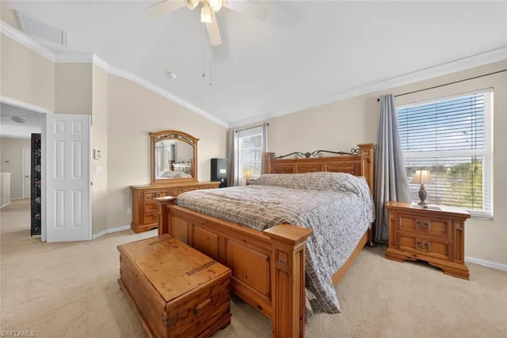 Primary bedroom featuring light colored carpet, lofted ceiling, ornamental molding, and ceiling fan