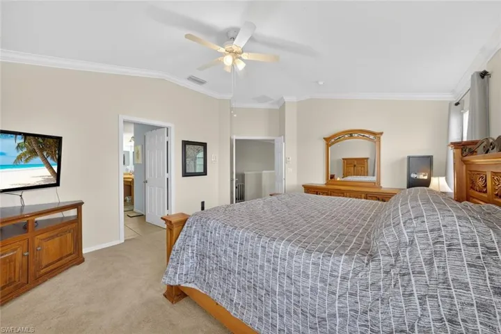 Primary bedroom with ornamental molding, light carpet, vaulted ceiling, ceiling fan, and ensuite bath
