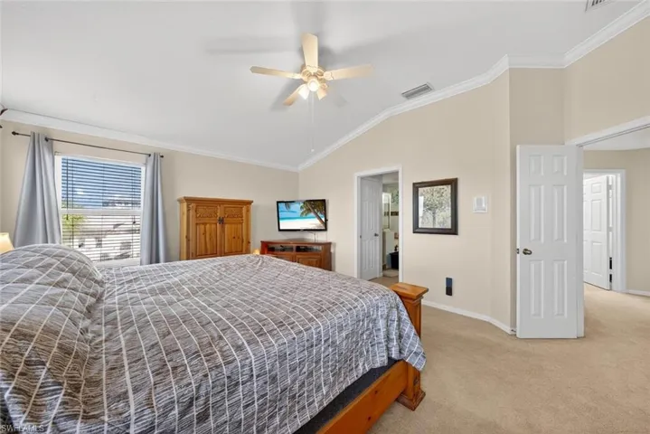 Primary bedroom with light colored carpet, vaulted ceiling, crown molding, and a ceiling fan