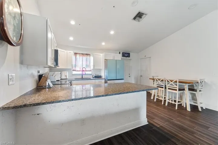 Kitchen with a peninsula, white cabinetry, freestanding refrigerator, dark stone counters, and recessed lighting