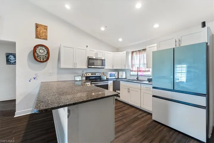 Kitchen with lofted ceiling, stainless steel appliances, white cabinets, a peninsula, and dark stone counters