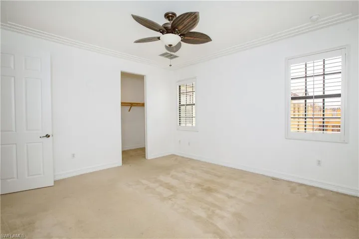 Unfurnished bedroom with carpet, a closet, ceiling fan, a walk in closet, plantation shutters, and ornamental molding
