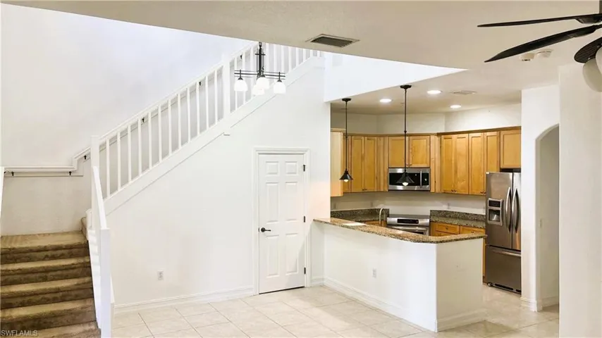Kitchen with appliances with stainless steel finishes, brown cabinetry, visible vents, ceiling fan, and dark stone counters