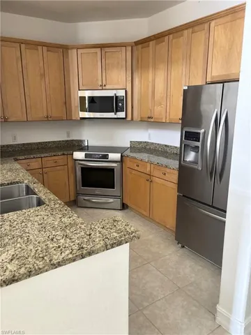 Kitchen featuring dark stone countertops, brown cabinets, light tile patterned floors, and appliances with stainless steel finishes