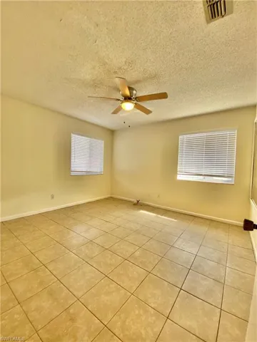 Empty room featuring light tile patterned floors, ceiling fan, plenty of natural light, and a textured ceiling
