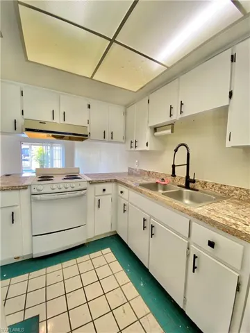 Kitchen featuring under cabinet range hood, electric range, white cabinets, and light countertops