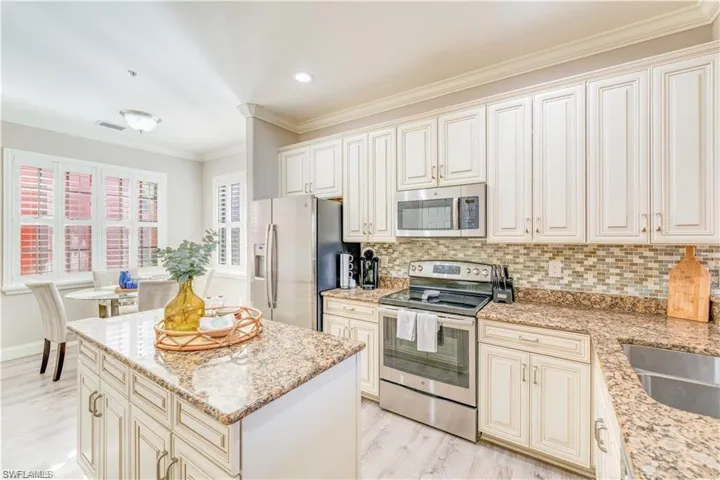 Kitchen featuring cream cabinets, stainless steel appliances, backsplash, ornamental molding, and light wood-style floors