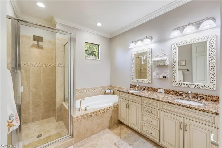 Bathroom featuring crown molding, a shower stall, a garden tub, light tile patterned floors, and double vanity