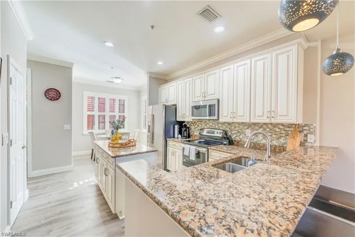Kitchen featuring a center island, appliances with stainless steel finishes, decorative backsplash, ornamental molding, and light stone countertops