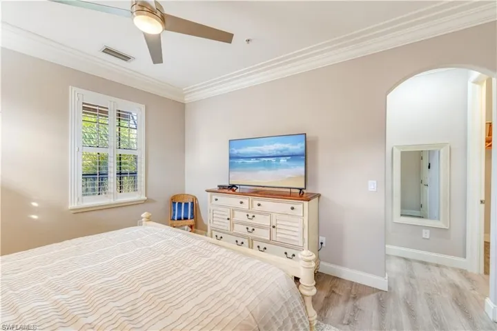 Bedroom with crown molding, light wood-style floors, a ceiling fan, and arched walkways