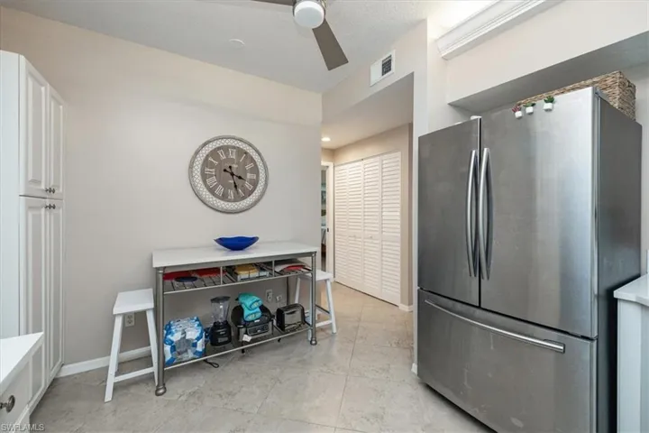 Kitchen featuring freestanding refrigerator, ceiling fan, white cabinetry, light tile patterned flooring, and light countertops