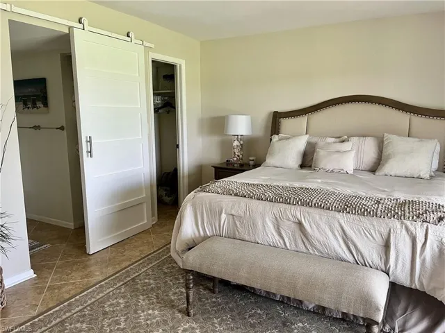 Tiled primary bedroom featuring a king bed with a barn door to bathroom and a spacious closet