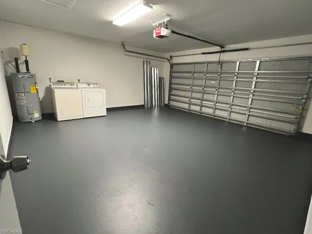 Garage featuring washing machine and dryer, a garage door opener, and water heater