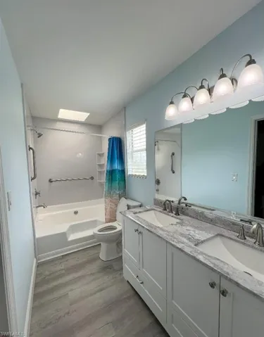 Full bathroom featuring dual bowl vanity, shower / bath combination with curtain, hardwood / wood-style floors, and toilet