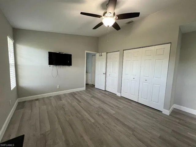 Unfurnished bedroom featuring ceiling fan, two closets, vaulted ceiling, and wood-type flooring