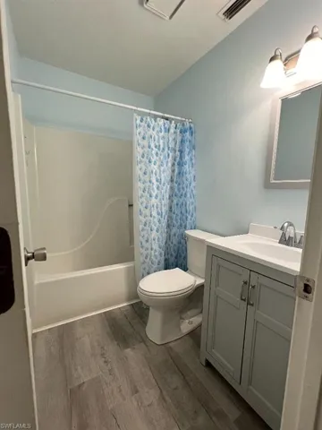 Full bathroom featuring wood-type flooring, toilet, shower / tub combo with curtain, and vanity
