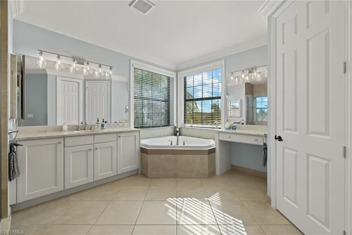 His Side and Her Side HUGE Bathroom with tiled bath, vanity, tile patterned floors, and crown molding