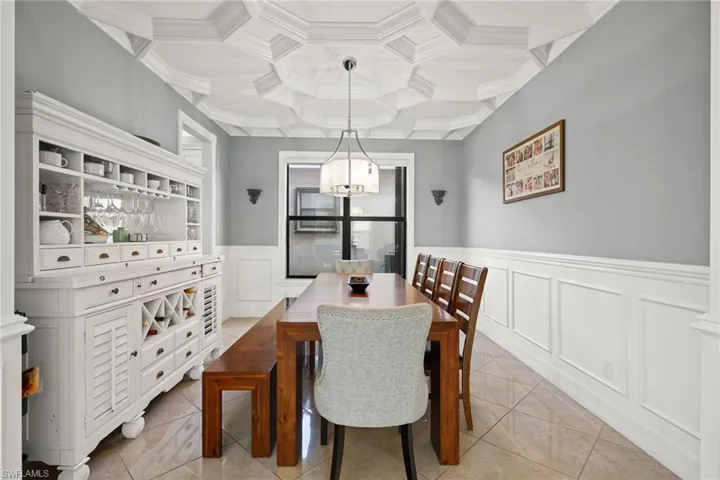 Tiled dining room featuring wall and crown molding, amazing coffered ceiling, decorative columns, and a chandelier