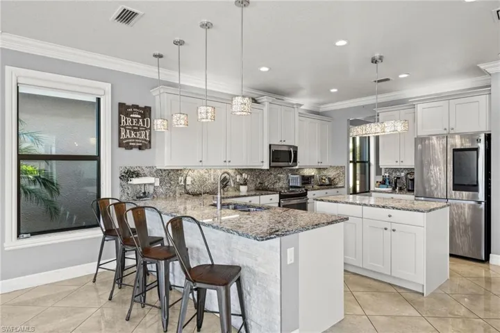 Kitchen with kitchen peninsula, appliances with stainless steel finishes, light stone counters, and hanging light fixtures