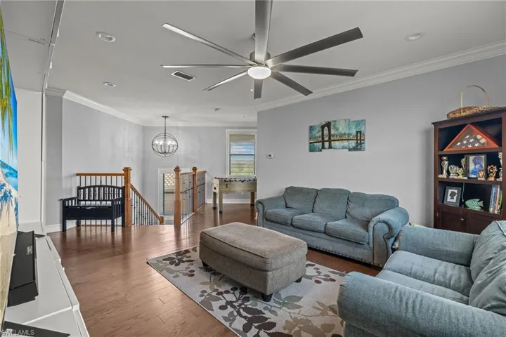 Loft with hardwood / wood-style floors, ceiling fan with notable chandelier, and crown molding