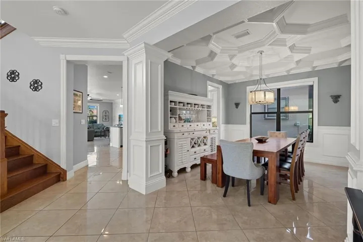 Exquisite dining room with ornate columns, custom coffered ceiling, ornamental molding, and ceiling fan with notable chandelier