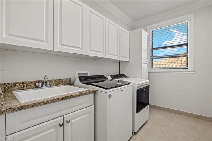 Clothes washing area with separate washer and dryer, cabinets, sink, light tile patterned floors, and ornamental molding