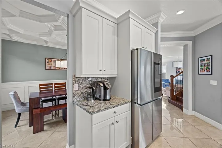 Kitchen with white cabinets, ornamental molding, light stone counters, and stainless steel upgraded refrigerator