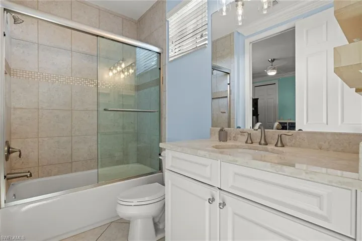 Full bathroom with tile patterned floors, toilet, ornamental molding, shower / bath combination with glass door, and vanity