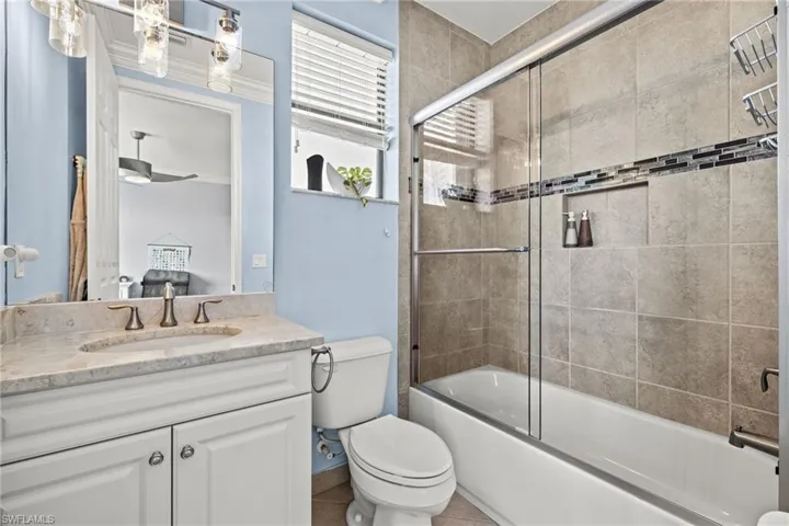Full bathroom with enclosed tub / shower combo, tile patterned floors, vanity, and toilet