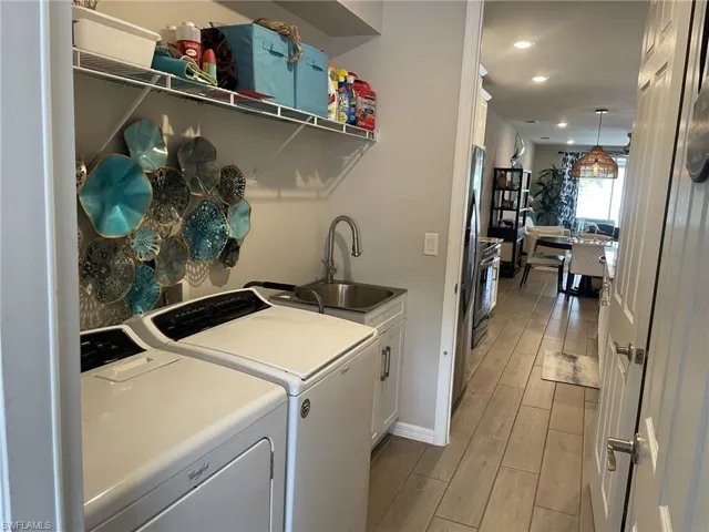 Clothes washing area with sink, light hardwood / wood-style flooring, separate washer and dryer, and cabinets