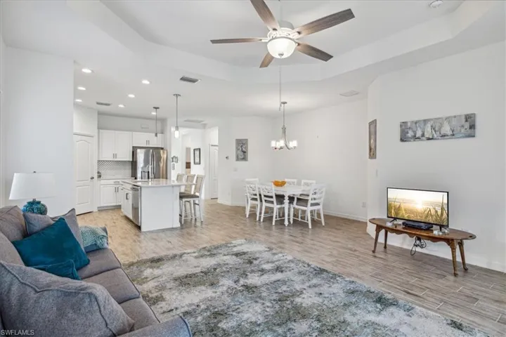 Living room featuring ceiling fan with notable chandelier, a tray ceiling, and light wood-type flooring