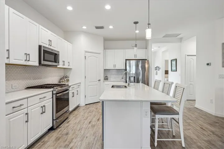 Kitchen featuring light hardwood / wood-style flooring, stainless steel appliances, backsplash, hanging light fixtures, and sink