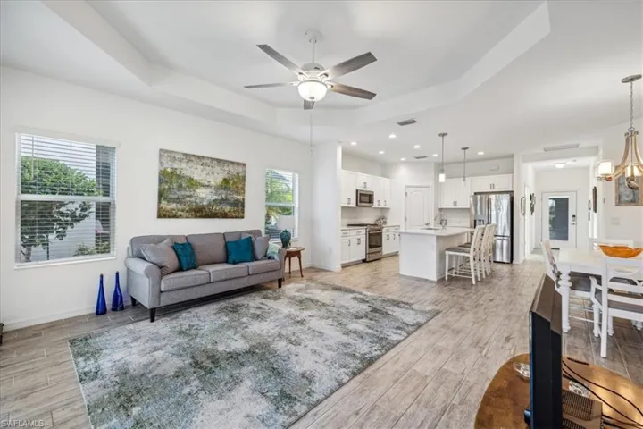 Living room with a raised ceiling, ceiling fan with notable chandelier, light hardwood / wood-style floors, and sink