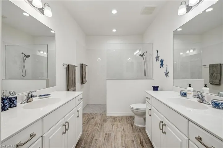 Bathroom with tiled shower, wood-type flooring, toilet, and vanity
