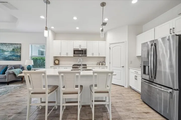 Kitchen with stainless steel appliances, backsplash, hanging light fixtures, an island with sink, and light wood-type flooring