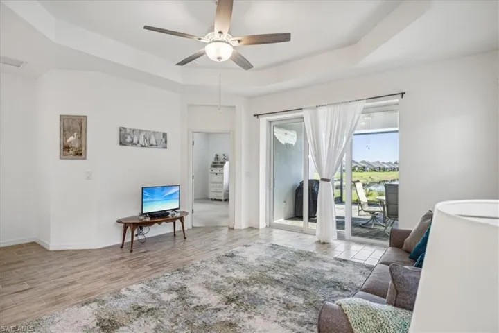 Living room featuring ceiling fan, a tray ceiling, and light hardwood / wood-style flooring