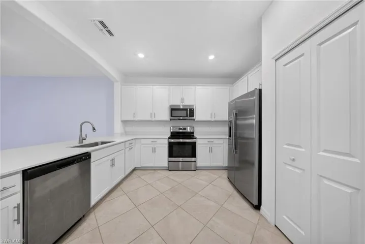Kitchen featuring stainless steel appliances, white cabinets, light tile patterned flooring, recessed lighting, and light stone counters