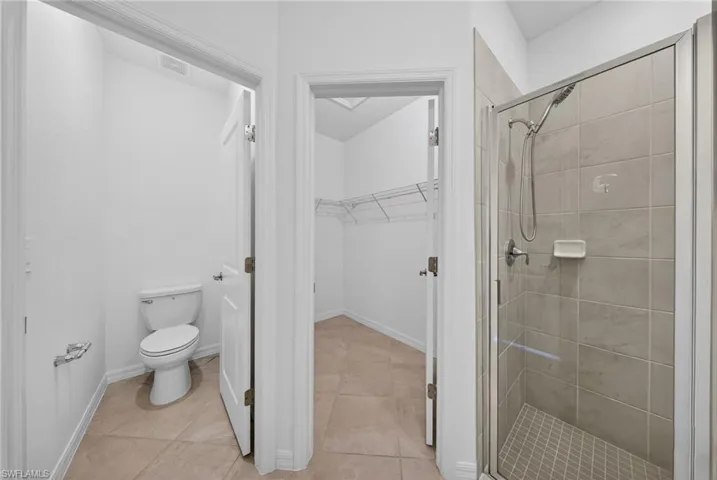 Bathroom with a walk in closet, a stall shower, and light tile patterned floors
