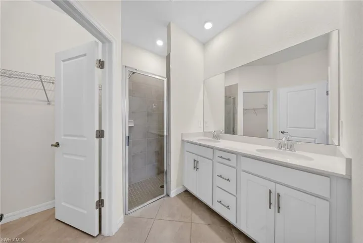 Full bathroom with a walk in closet, double vanity, a stall shower, and light tile patterned floors