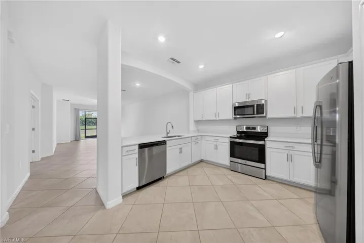 Kitchen featuring white cabinets, stainless steel appliances, light countertops, arched walkways, and recessed lighting