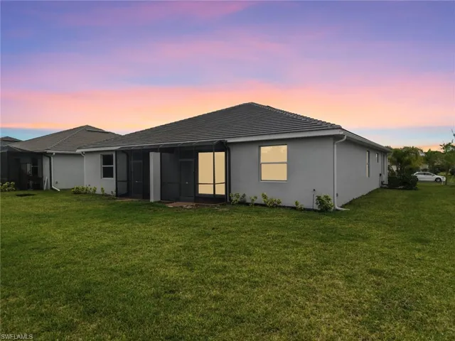 Back of house at dusk featuring a lawn, a sunroom, and stucco siding