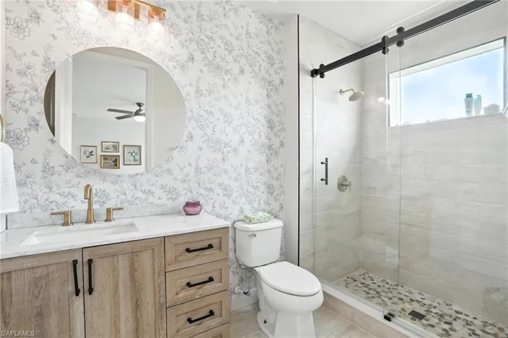 Bathroom with wallpapered walls, vanity, a stall shower, and a ceiling fan