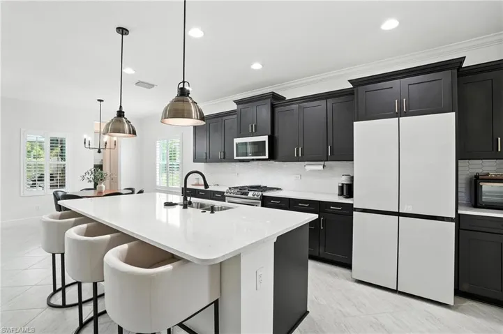 Kitchen featuring white appliances, a center island with sink, tasteful backsplash, dark cabinets, and a kitchen breakfast bar