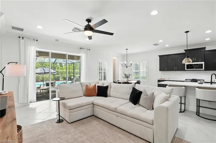 Living area with crown molding, ceiling fan, recessed lighting, light tile patterned floors, and a chandelier