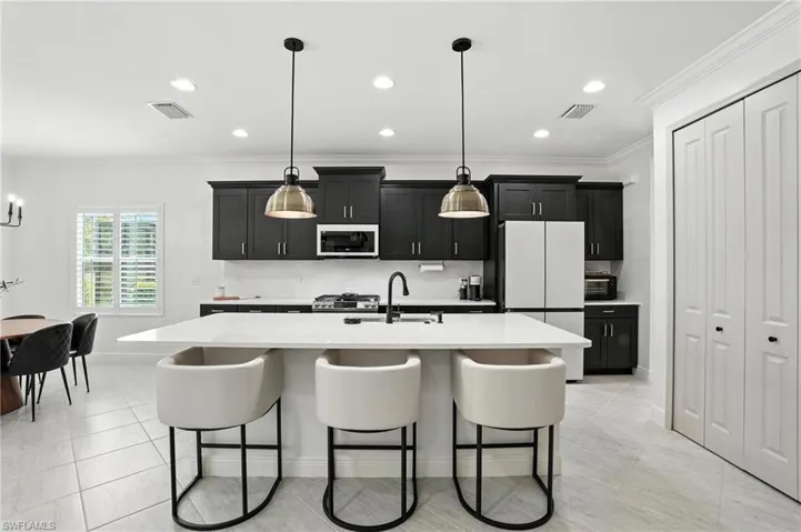 Kitchen featuring white appliances, dark cabinetry, light countertops, a breakfast bar area, and ornamental molding