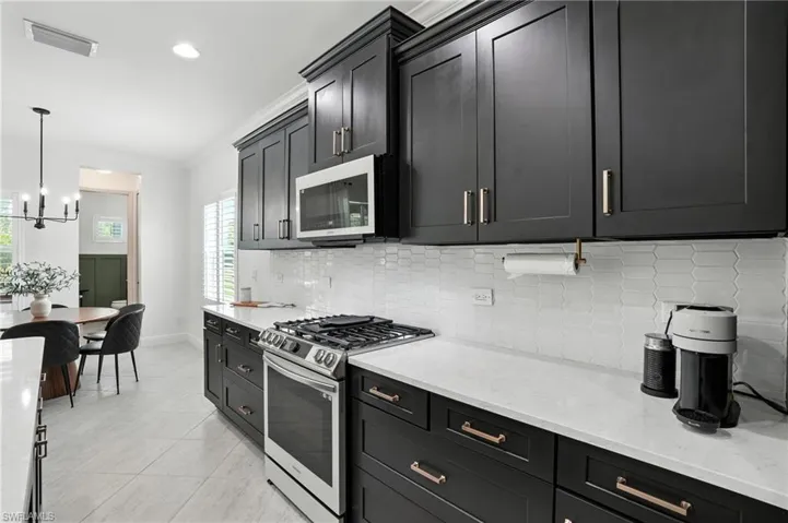 Kitchen featuring stainless steel gas range, crown molding, backsplash, a chandelier, and dark cabinetry