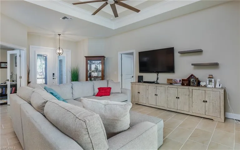 Living room with double tray ceiling, light tile patterned floors, ceiling fan with crown molding