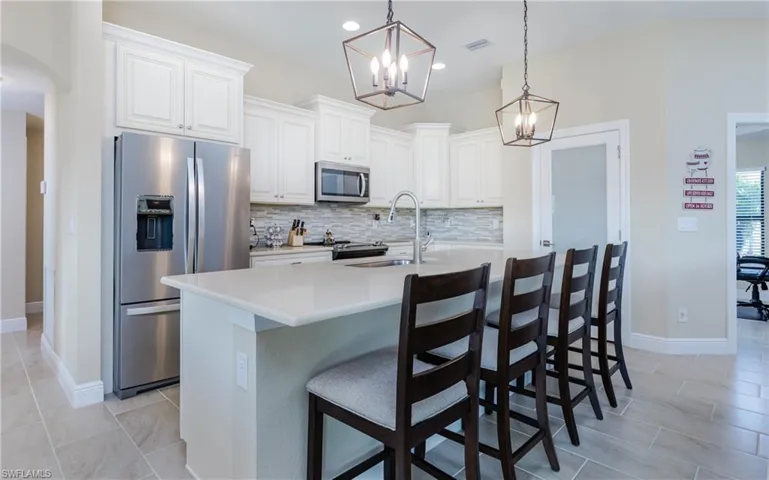 Kitchen with custom  cabinetry, sink, decorative light fixtures, a kitchen island with sink, and appliances with stainless steel finishes